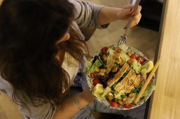 Overhead view of a woman eating a chicken salad balancing health with deliciousness.
